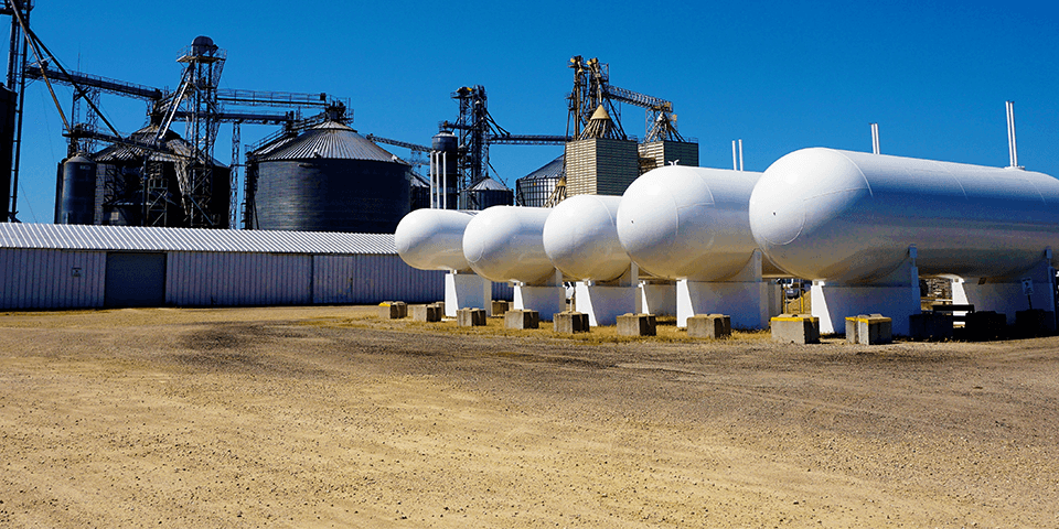 A row of commercial propane tanks with a production plant behind them